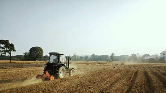 圖為機(jī)耕手正在使用大型拖拉機(jī)對煙田旋耕起壟