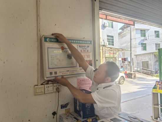 圖為稽查員幫助零售戶懸掛煙草專賣零售許可證